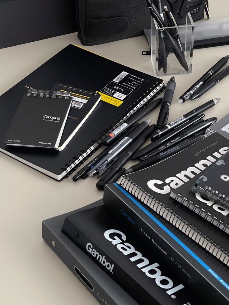 several notebooks and pens are sitting on a table next to a black book bag