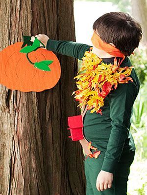 a young boy dressed in green and orange standing next to a tree with a paper pumpkin on it