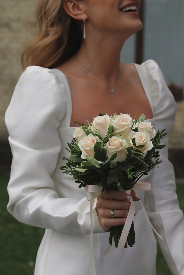 a woman wearing a white dress holding a bouquet of flowers in her hand and laughing