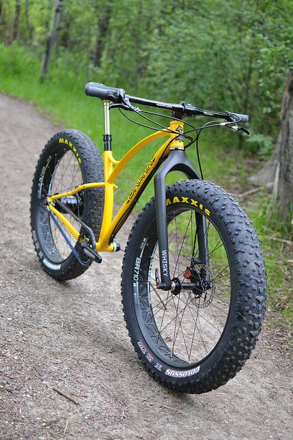 a yellow bike parked on the side of a dirt road in front of some trees