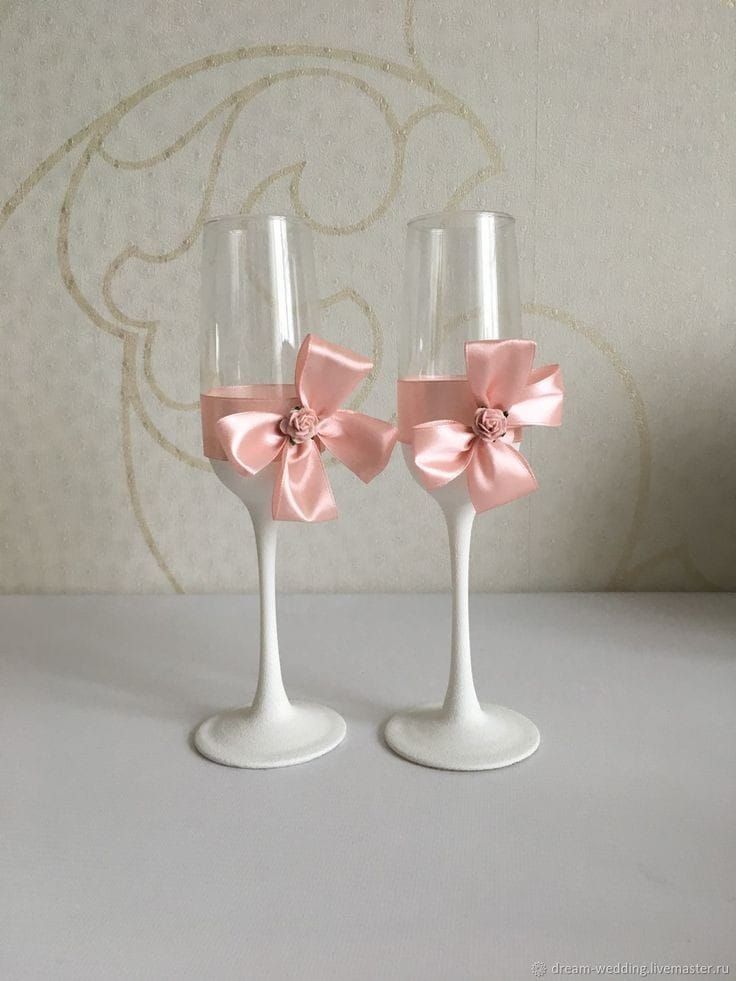 two wine glasses with pink bows on them sitting next to each other in front of a wall