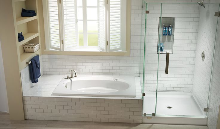 a bath tub sitting under a window next to a sink and shower stall in a bathroom