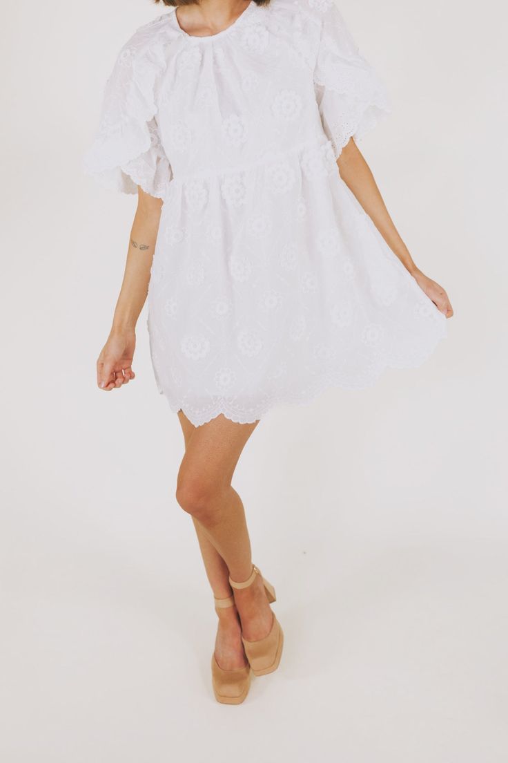 This white embroidered floral mini dress is the epitome of romantic elegance. Featuring a delicate scallop hemline and ruffle lace details, it is the perfect addition to any summer wardrobe. Enhance your feminine charm and steal hearts wherever you go with this beautiful dress. Details Round neckline Keyhole closure Ruffle lace details Embroidered fabricaiton Scallop hemline Lined Pockets Sizing Approximate measurements: SIZE LENGTH BUST WAIST Small 33” 36” 36” Medium 33” 38” 38” Large 34” 40” 4 Flowy Lace Dresses With Floral Embroidery, Flirty Lace Mini Dress For Spring, Flirty Spring Mini Dress With Scalloped Lace, Chic Mini Lace Dress With Ruffles, Summer Scalloped Lace Mini Dress, Flirty Lace Dress For Garden Party, Daywear Mini Dress With Scalloped Lace, Lace Mini Dress With Floral Embroidery For Garden Party, Spring Chic Lace Dress With Scalloped Edges