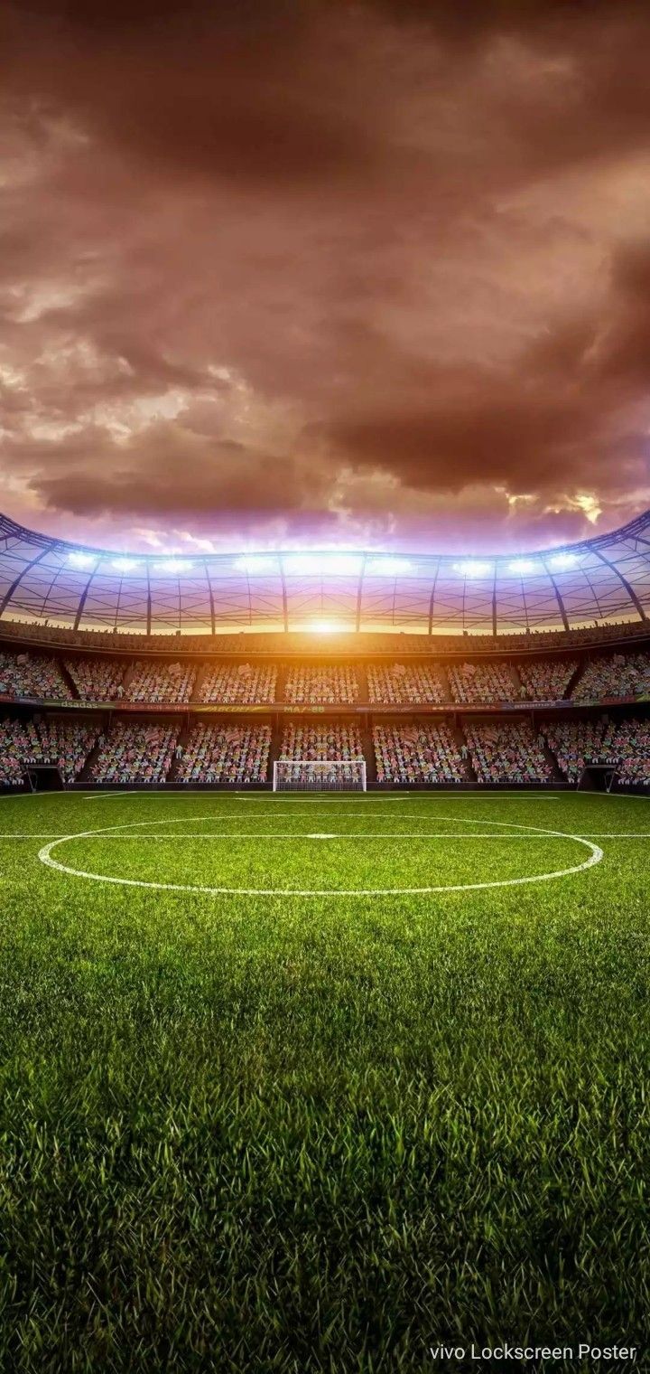 an empty soccer field in front of a large stadium with the sun shining down on it