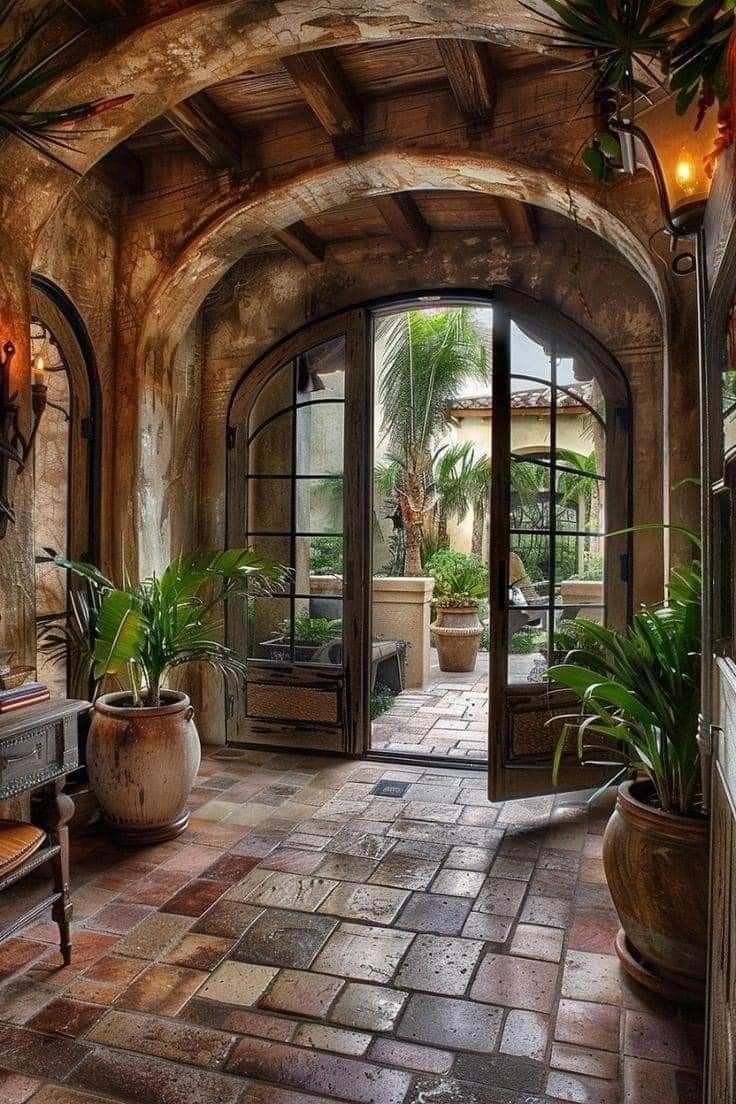 an arched entry way with potted plants on either side and glass doors leading to another room