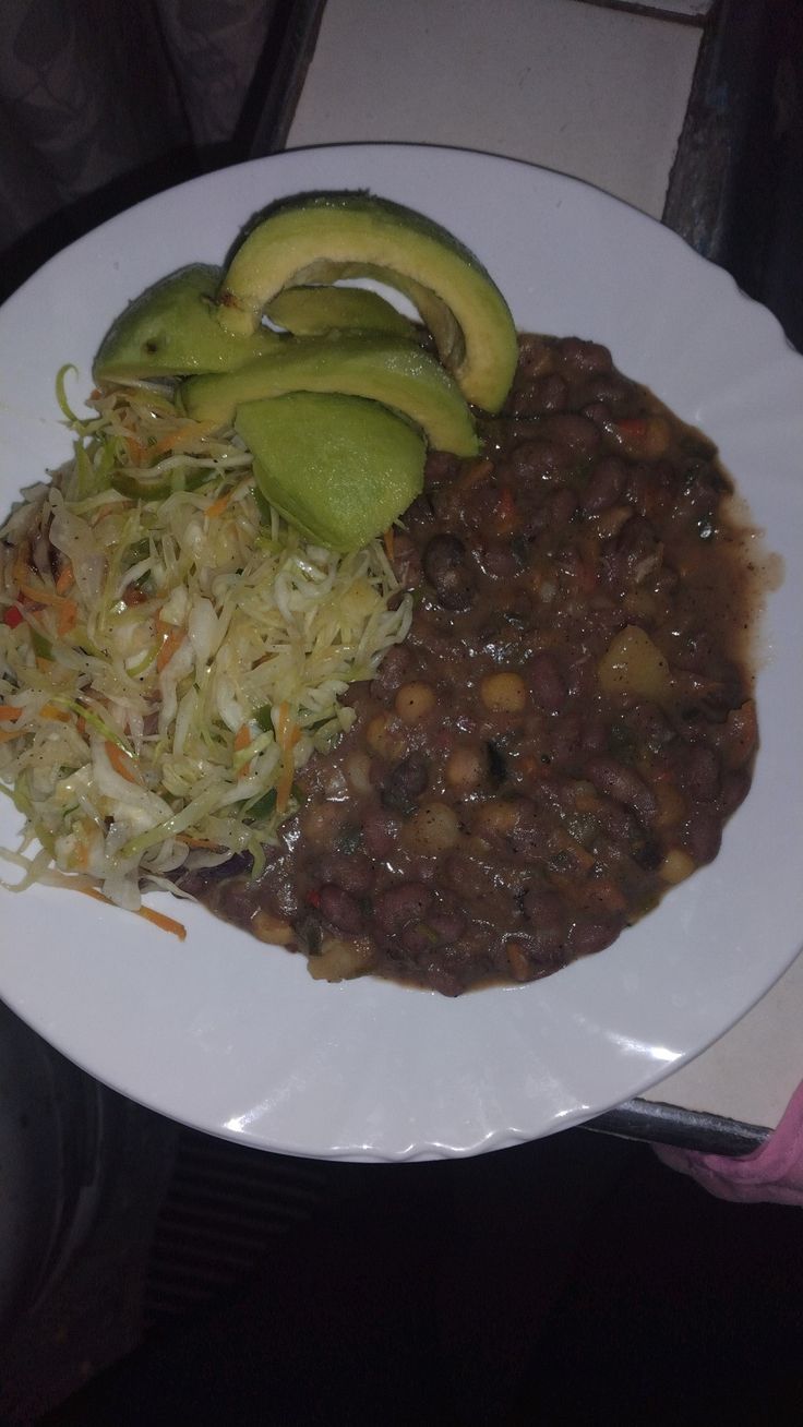 a white plate topped with beans and veggies next to an avocado