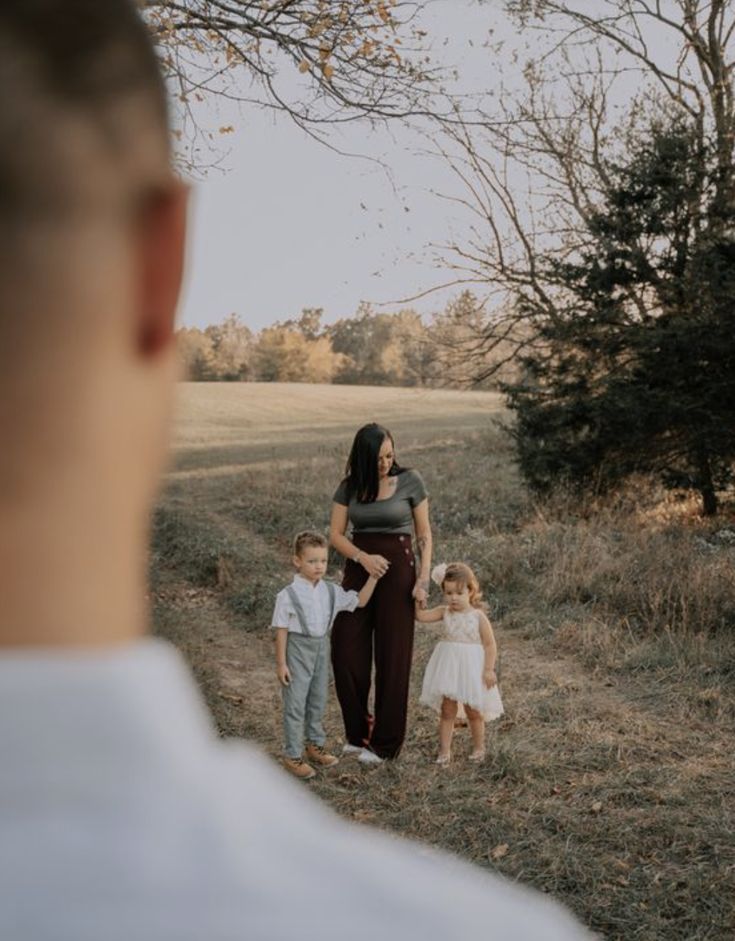 a woman and two children are standing in the grass with their mother looking at them