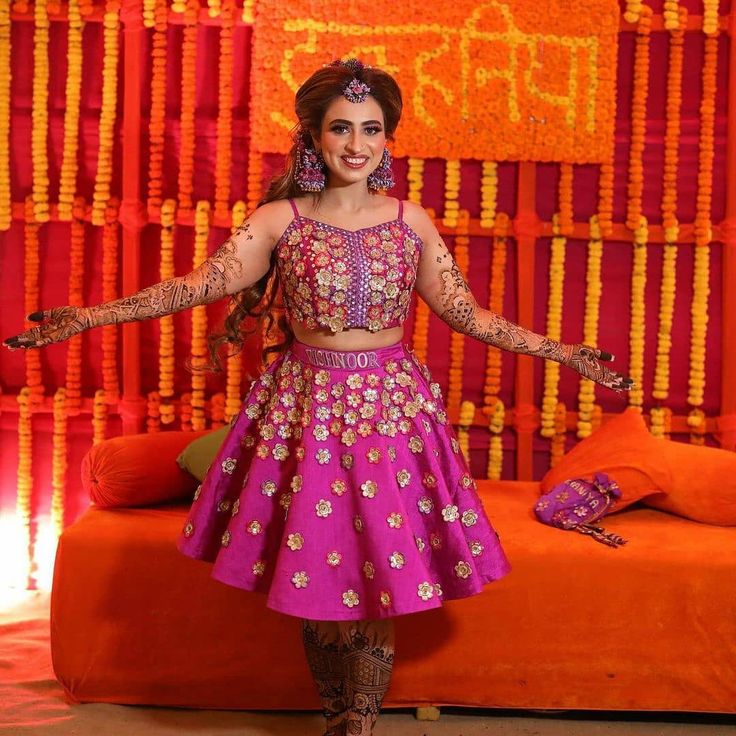 a woman in a pink and gold outfit standing next to an orange couch with her arms outstretched