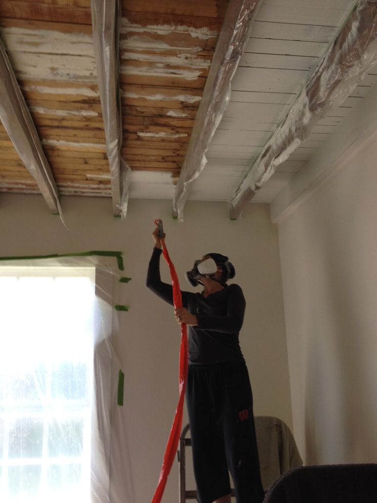 a man is using a hose to clean the ceiling in his room with no curtains