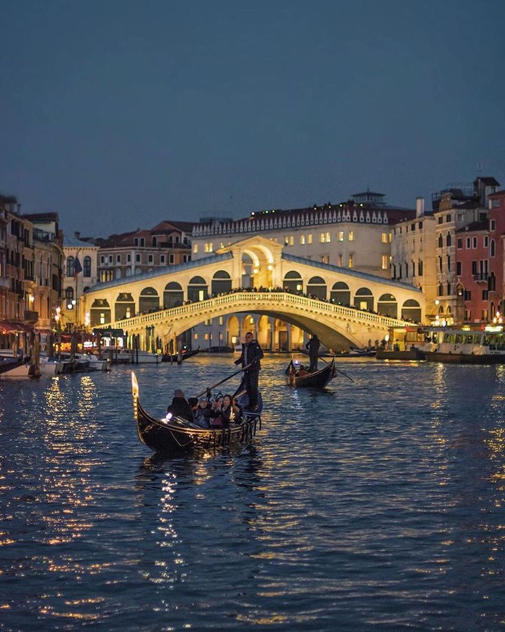 two gondolas on the water in front of a bridge and buildings at night