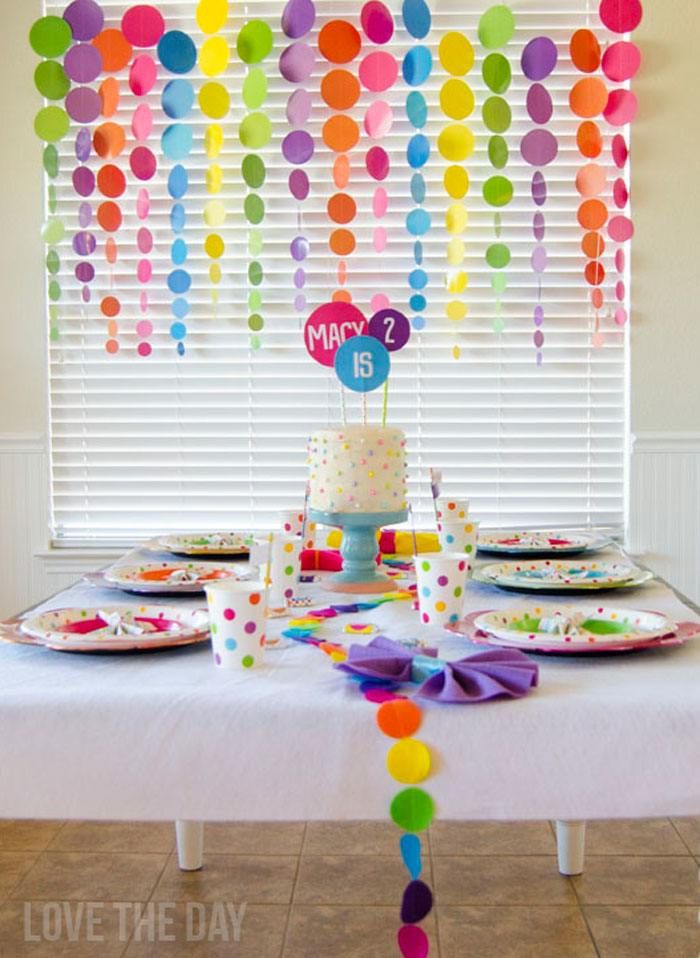 a table with plates and cups on it in front of a window that has balloons hanging from the ceiling