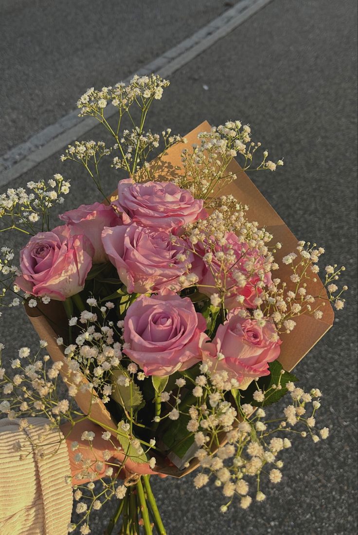 a person holding a bouquet of pink roses and baby's breath