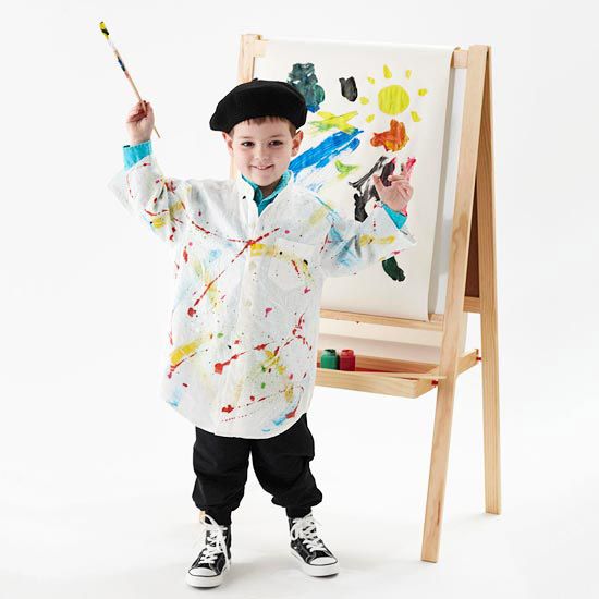 a young boy is standing in front of an easel and holding a paintbrush