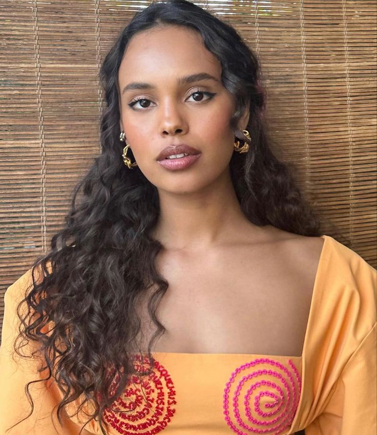 a woman with long hair wearing an orange top and gold hoop earrings is posing for the camera