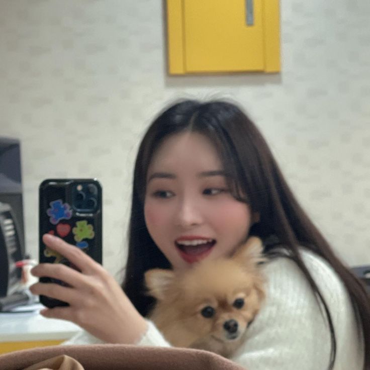 a woman holding a small dog in her lap while looking at her cell phone and taking a selfie