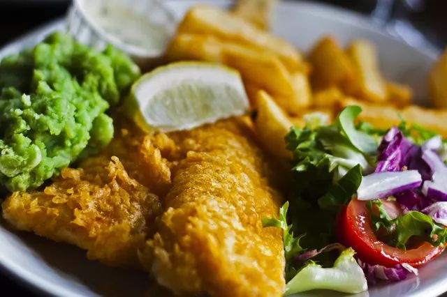 a white plate topped with fried fish and french fries next to veggie salad