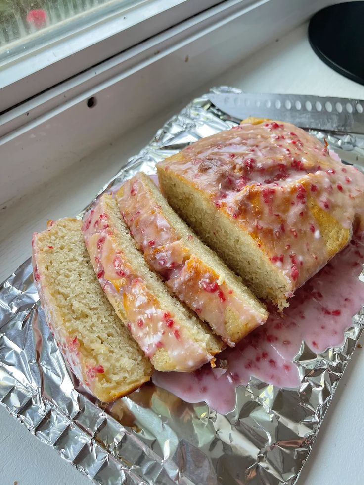 a loaf of cake sitting on top of aluminum foil covered in pink icing and sprinkles