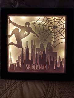 an illuminated shadow box with a spiderman silhouette in the center and city lights behind it