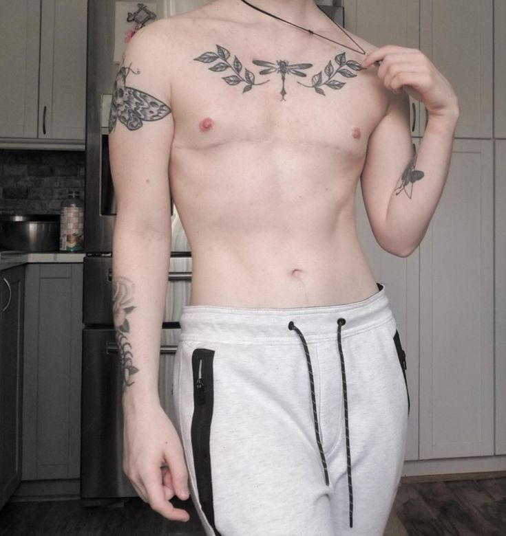 a shirtless man with tattoos on his chest standing in front of a kitchen counter