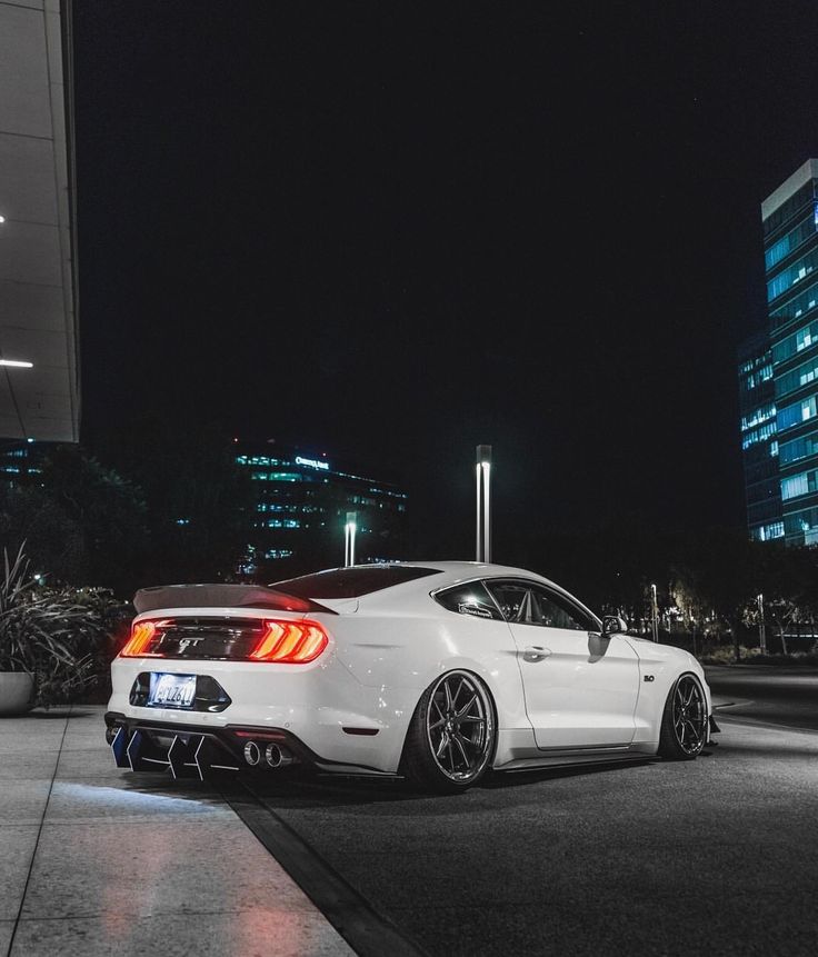 a white car parked in front of a tall building at night with its lights on