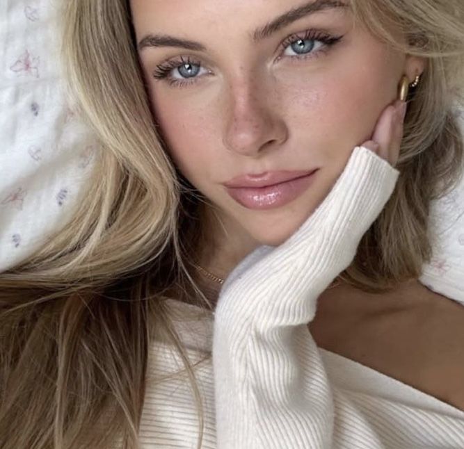 a woman laying on top of a bed next to a white blanket and wearing a sweater