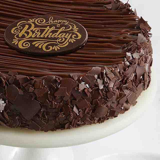 a birthday cake with chocolate frosting and decorations on it's top, sitting on a white pedestal