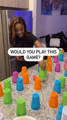 a woman standing in front of a table filled with cups and plastic cups that say would you play this game?