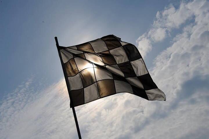 a black and white checkered flag flying in the sky with sun shining behind it