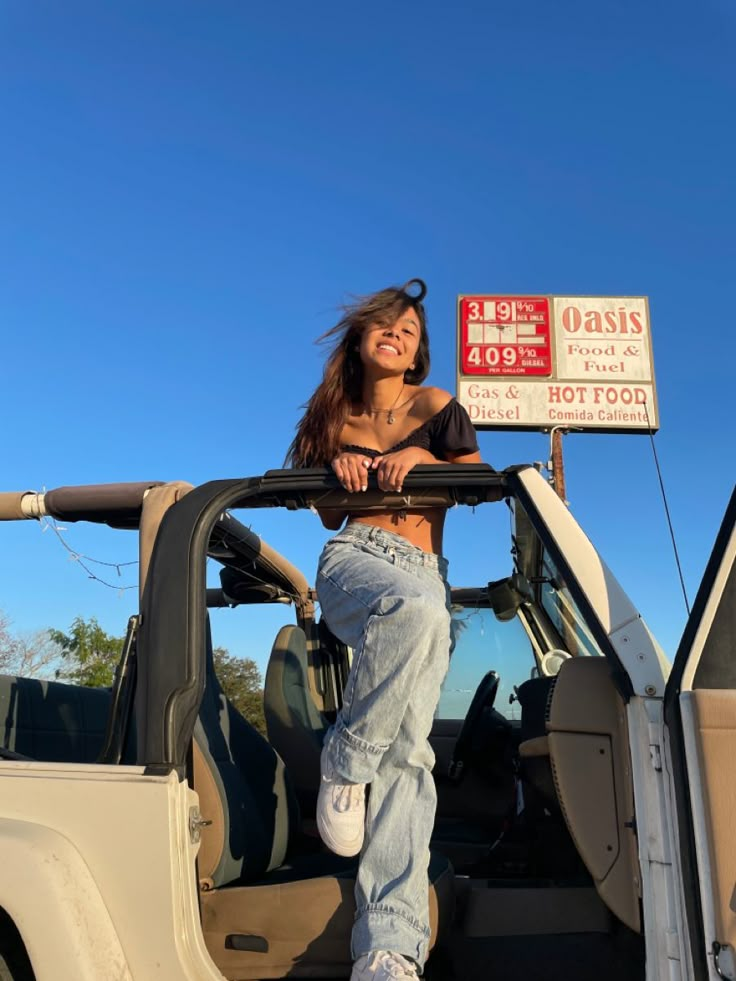 a woman sitting in the back of a truck next to a gas pump and sign