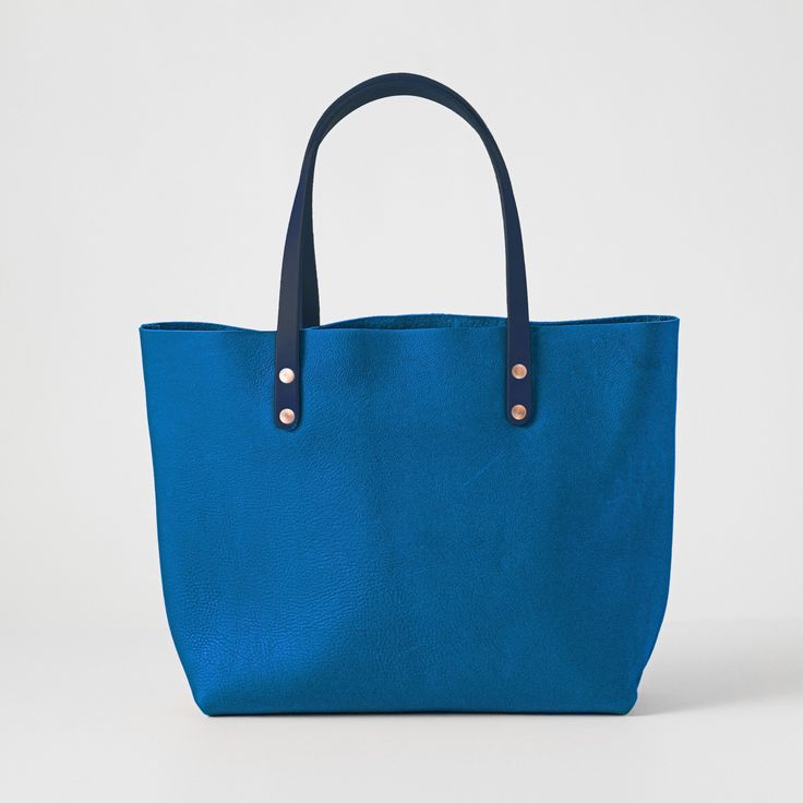 The Cerulean Cypress East West Tote is a large leather tote bag handmade in the USA with heirloom-quality craftsmanship and the very best materials. Cerulean Cypress is a thick and soft leather with a pillowy texture, even bright blue color, little to no pull-up, and pebbled grain. The Cerulean Cypress East West Tote comes standard with Navy handles. Blue Top Handle Shoulder Bag With Leather Lining, Rectangular Blue Shoulder Bag With Leather Lining, Blue Rectangular Shoulder Bag With Rolled Handles, Blue Top Handle Bag With Leather Lining, Blue Bag For Daily Use With Smooth Grain, Modern Blue Bags With Rolled Handles, Blue Smooth Grain Bag For Daily Use, Blue Textured Leather Tote Shoulder Bag, Modern Blue Bags With Smooth Grain