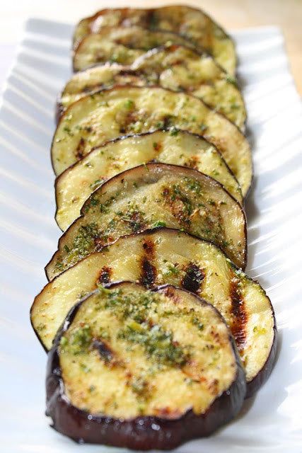 grilled eggplant slices are arranged on a white platter, ready to be eaten