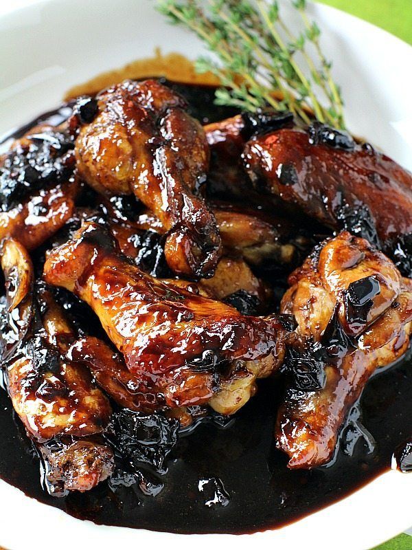 chicken wings with sauce on a white plate next to a sprig of rosemary