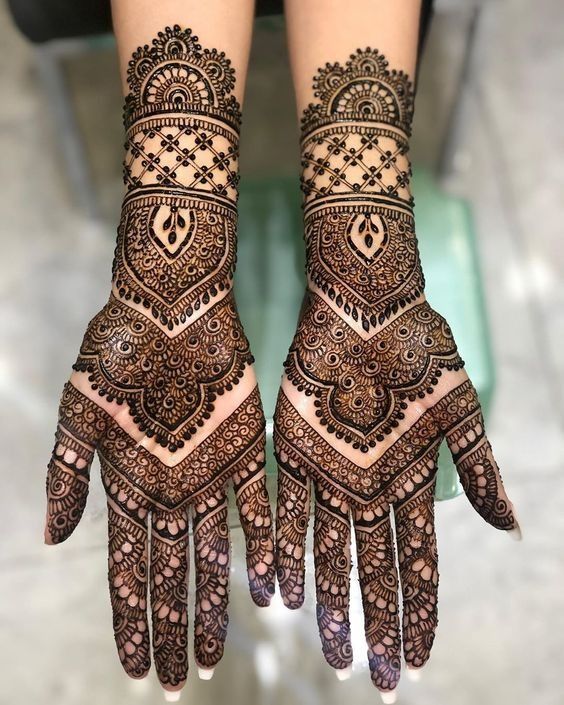 two hands with henna tattoos on them, one is showing the intricate pattern and the other has an elaborate design