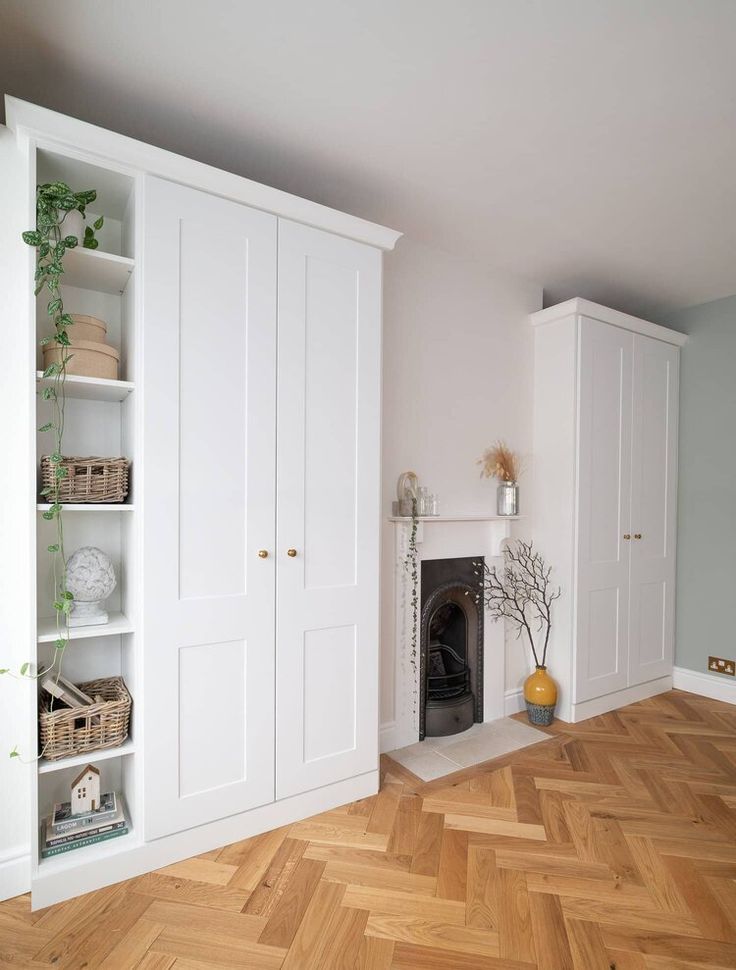 an empty room with white cupboards and a fireplace in the center, surrounded by wood flooring