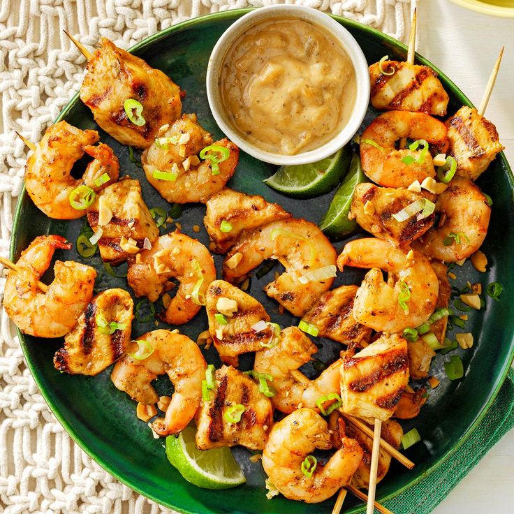 grilled shrimp skewers on a green plate with dipping sauce