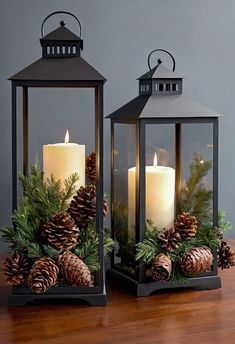 two black lanterns with pine cones and evergreens on them are sitting on a wooden table