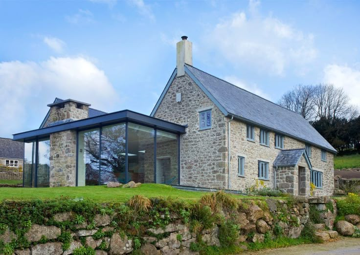 a stone house with a glass wall and windows on the front, surrounded by green grass