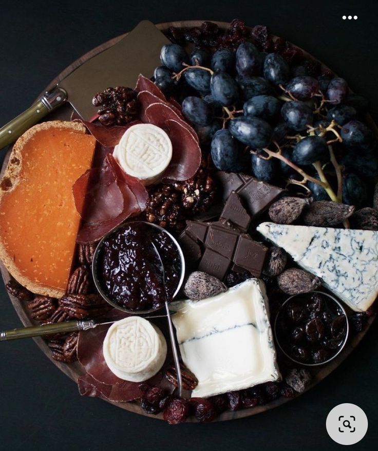 an assortment of cheeses, crackers and grapes on a plate