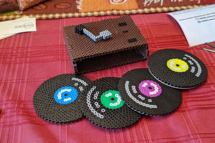 four black coasters with designs on them sitting on a red table cloth next to a brown box