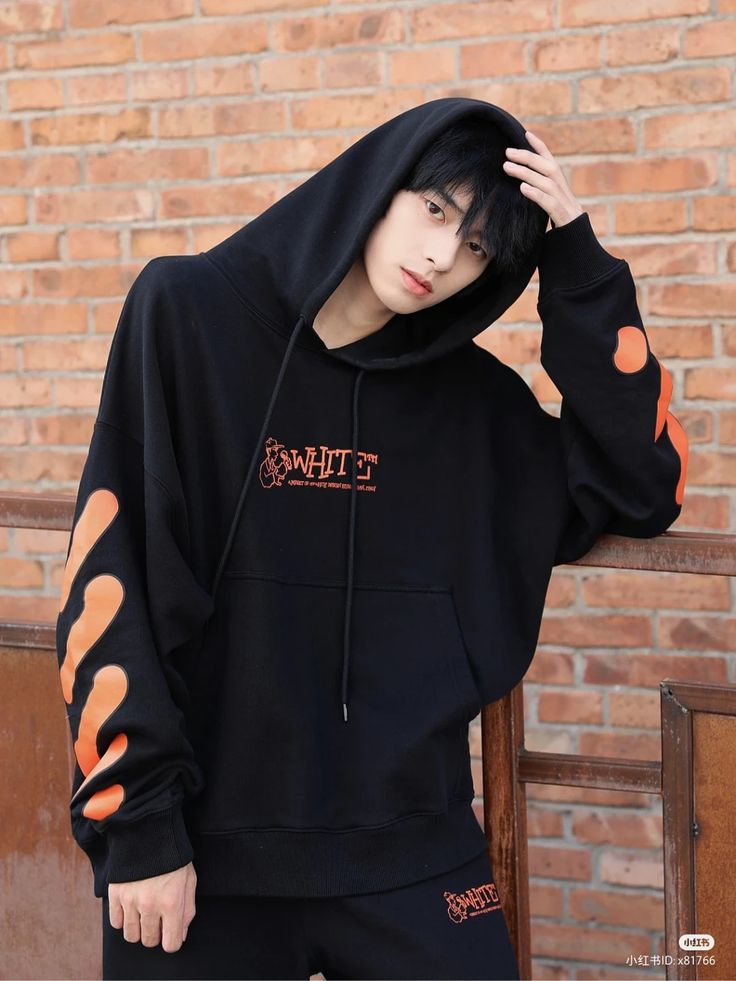 a young man wearing a black hoodie with orange spots on the sleeves and chest