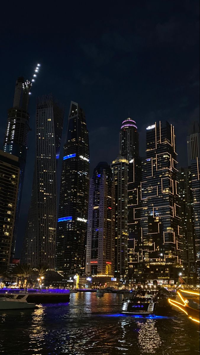 the city skyline is lit up at night with lights reflecting in the water and boats on the river