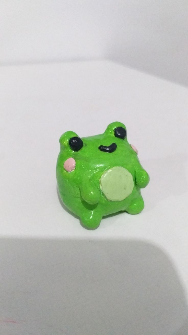 a small green frog toy sitting on top of a white surface with its eyes closed