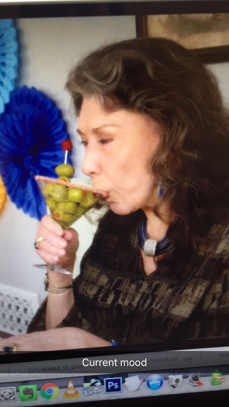 a woman drinking from a martini glass while sitting in front of a laptop computer screen