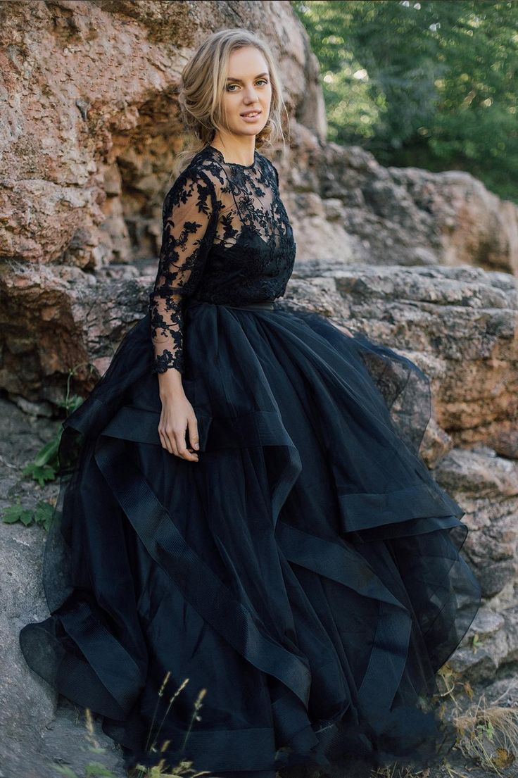 a woman in a black dress standing on some rocks