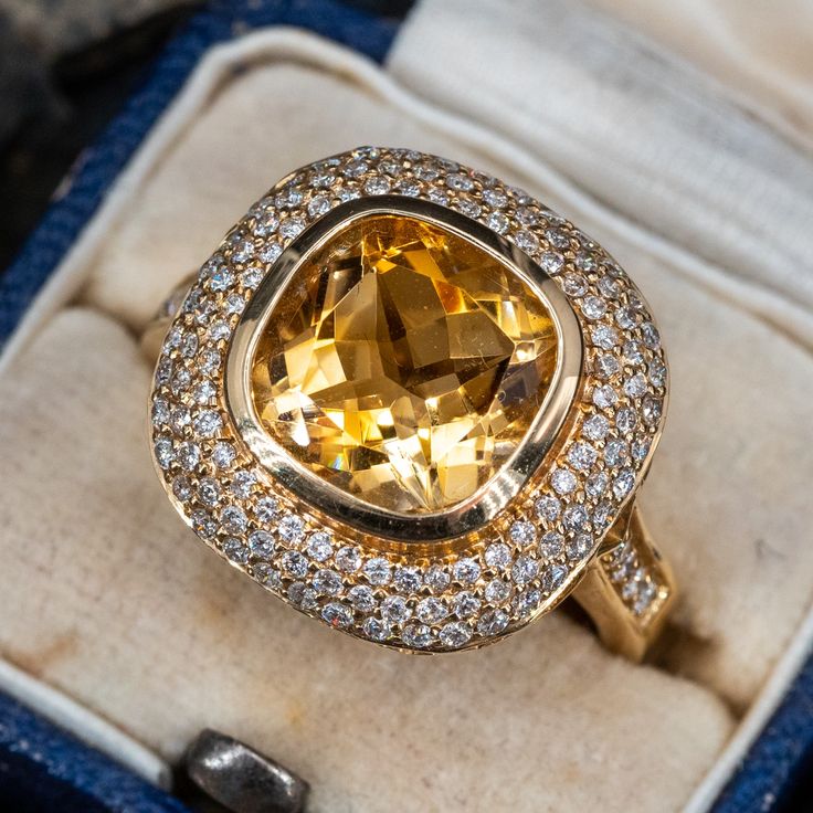 This alluring ring is centered with one (1) cushion mixed cut natural citrine set into a bezel setting. The diamond is bordered with one hundred fourteen (114), bead set, round brilliant cut diamonds. The top face of the shank is accented with a row of four (4), bead set, round brilliant cut diamonds. The ring measures 16.8mm at the top, rises 8.1mm above the finger, tapering to 2.7mm wide and 1.5mm thick at the base of the shank. This ring is currently a size 7. Citrine Ring Engagement, Vintage Cocktail Ring, Peridot Jewelry, Rings Collection, Engagement Rings Bridal Sets, Diamond Cocktail Rings, Bead Set, Citrine Ring, Yellow Citrine