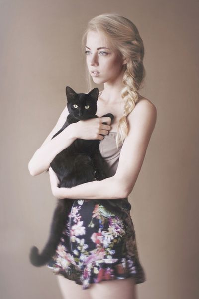 a young woman holding a black cat in her right hand and posing for the camera