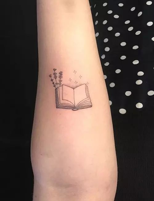 a small tattoo on the arm of a woman with an open book and flowers in it