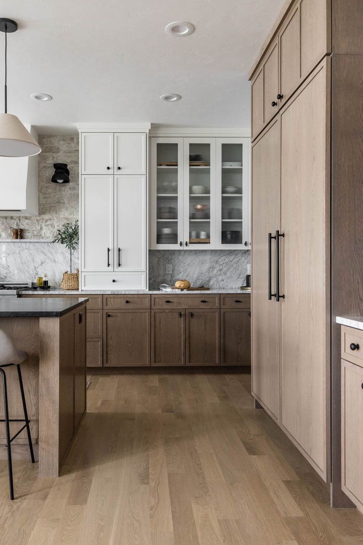 a kitchen with wooden floors and white cabinets, an island in the middle is surrounded by bar stools