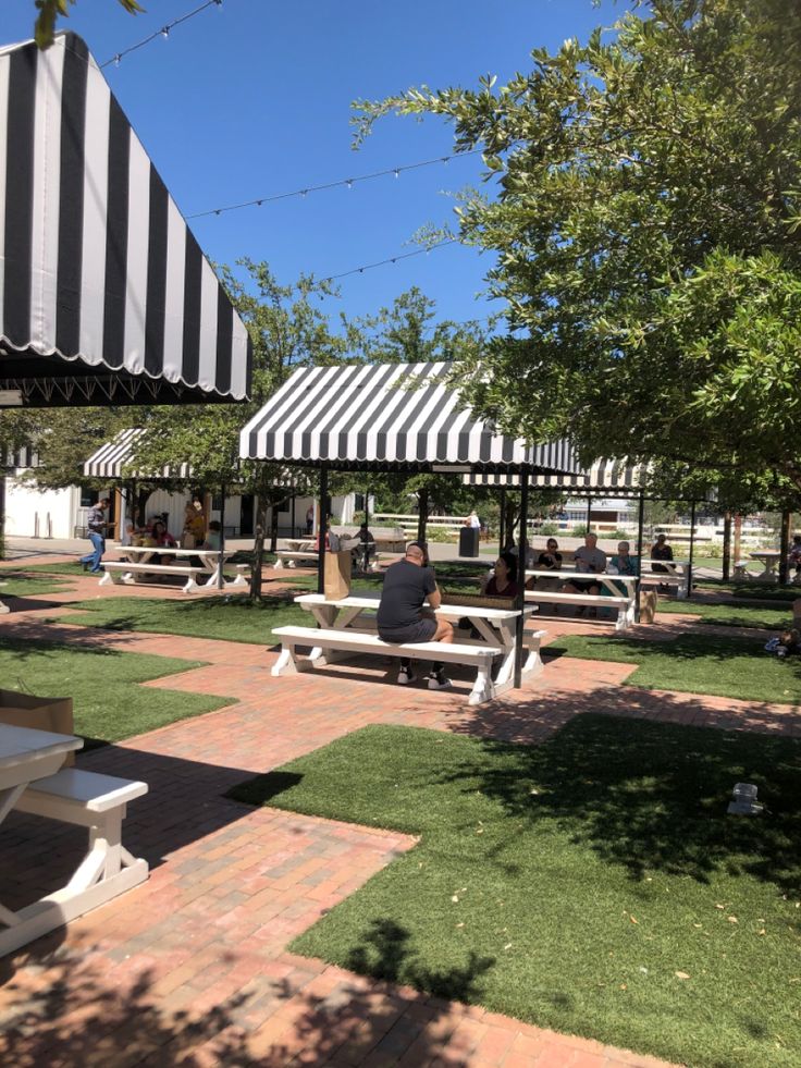 people are sitting on benches under the awnings at an outdoor picnic area with grass