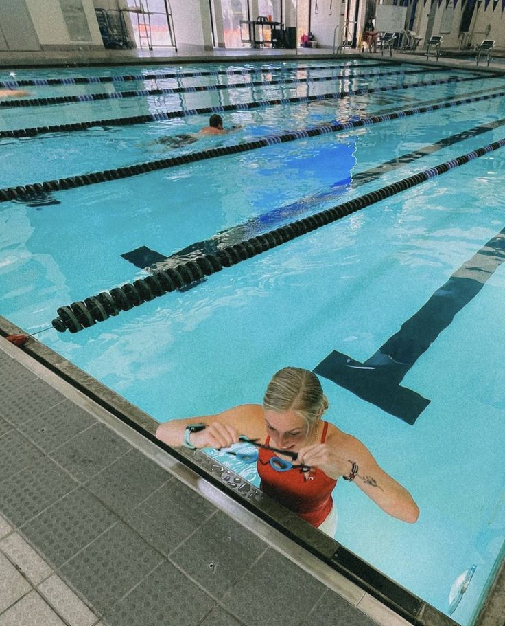 a woman in a red shirt is sitting on the edge of a swimming pool and looking at her cell phone